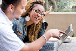 A male pupil tips to a persuasive essay on his laptop; he could be trying to convince women student to see his argument.